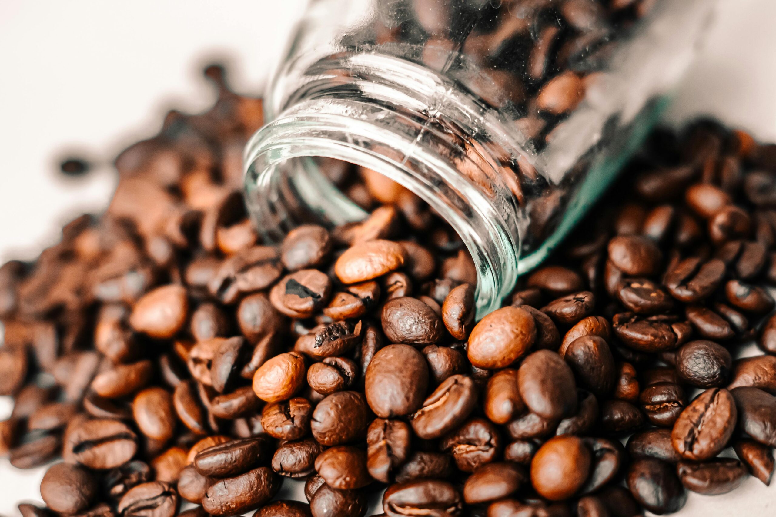 A detailed shot of aromatic coffee beans spilling from a transparent glass jar onto a surface.